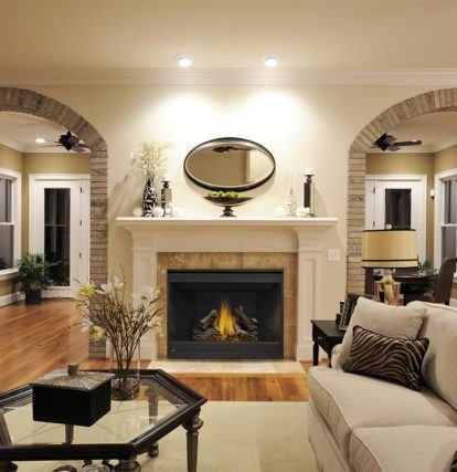 a bright furnished living room with a lit fireplace between two archways leading to other rooms