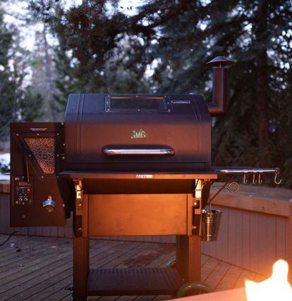 a smoker BBQ with wood pellet attachment on a backyard patio at dusk