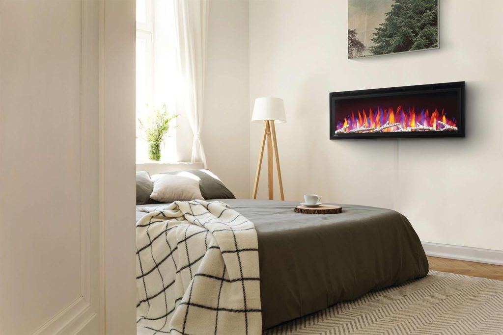 an electric fireplace mounted on the wall of a bedroom beside the bed